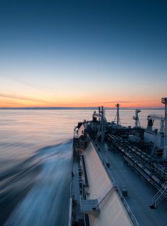 Liquigied natural gas tanker sails towards the sunset. Long exposure photo. Sun Light reflections are on the water. Blue sky with beautiful sunset sky and colors.